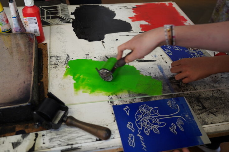 Kinderhände rollen Farbe auf ihr geschnitztes Bild. 