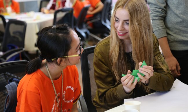 Eine deutsche und eine chinesische Schülerin sitzen an einem Tisch und sprechen miteinander