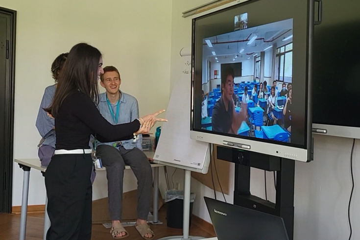 Drei Personen schauen auf einen Fernseher mit einem Videocall