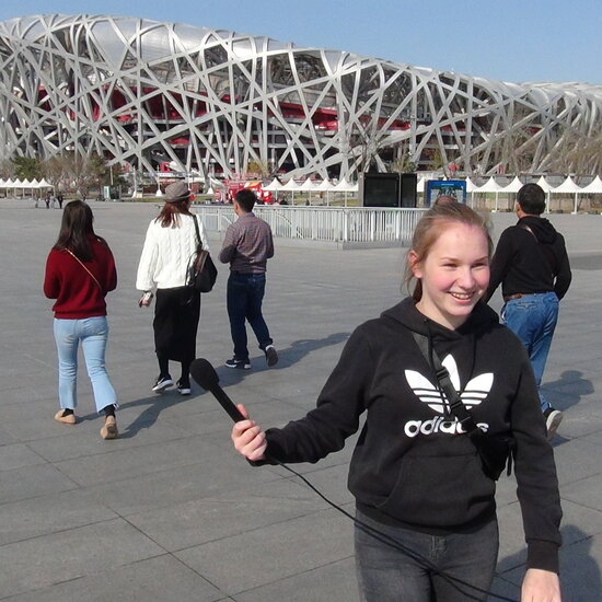 Eine Schülerin steht vor einem Sportstadion in Peking