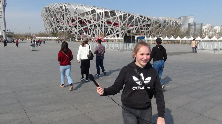Eine Schülerin steht vor einem Sportstadion in Peking