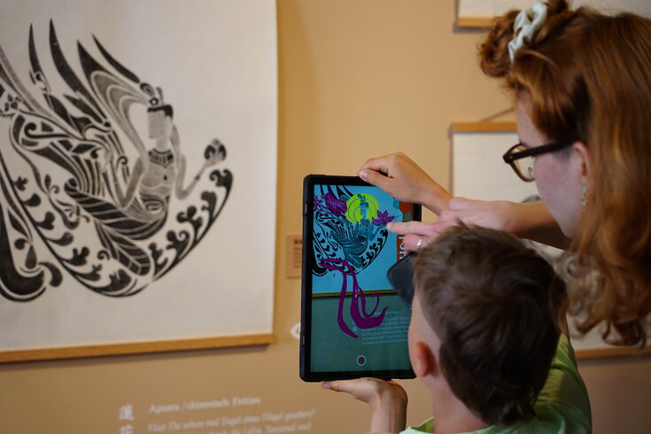 Frau und Kind scannen mit der Fotokamera eines Tablets ein Druckgemälde, um weitere Informationen zur Kunst zu erhalten.