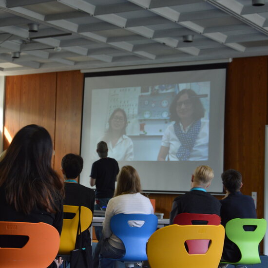 Ein Kurs mit Schüler:innen blickt auf eine Leinwand mit einem Videocall