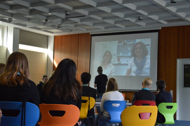 Ein Kurs mit Schüler:innen blickt auf eine Leinwand mit einem Videocall